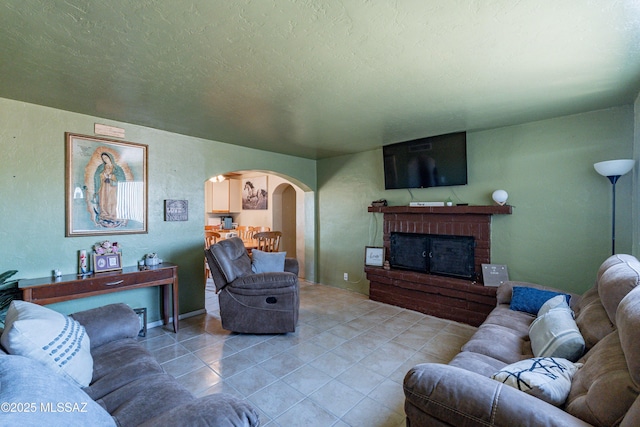 living area featuring a textured ceiling, a brick fireplace, arched walkways, a textured wall, and light tile patterned floors