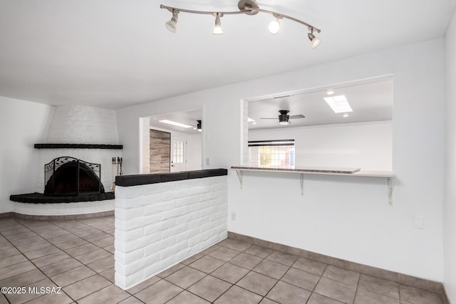kitchen with light tile patterned flooring, a breakfast bar, baseboards, a fireplace, and a ceiling fan