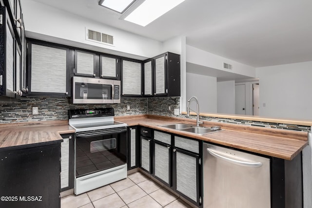 kitchen with backsplash, a sink, visible vents, a peninsula, and appliances with stainless steel finishes