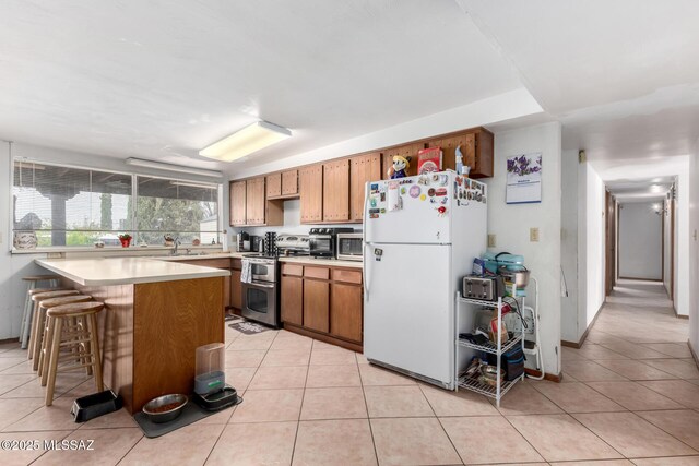 kitchen featuring light countertops, double oven range, light tile patterned flooring, freestanding refrigerator, and brown cabinetry