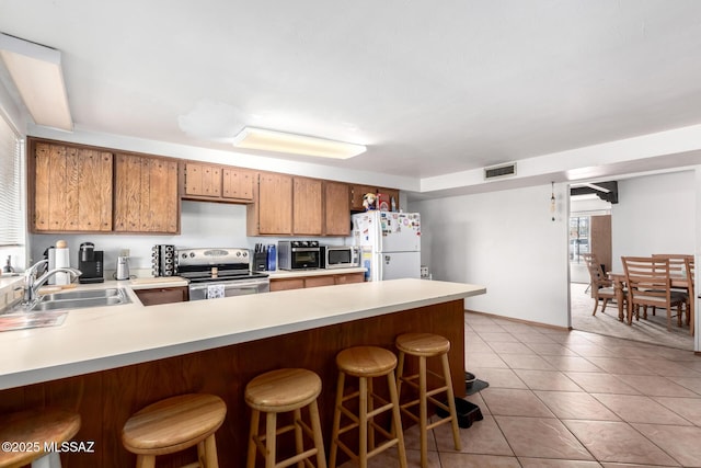kitchen with light countertops, a sink, a peninsula, stainless steel appliances, and visible vents