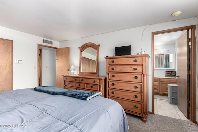 bedroom with light tile patterned flooring, connected bathroom, visible vents, and light carpet