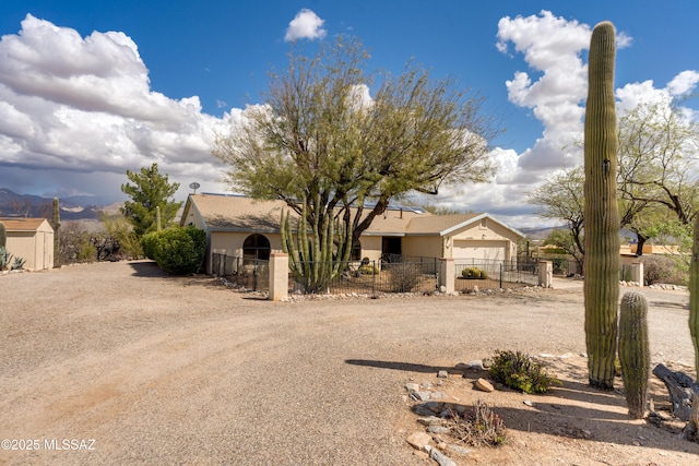 view of front facade featuring dirt driveway, stucco siding, an attached garage, and a fenced front yard