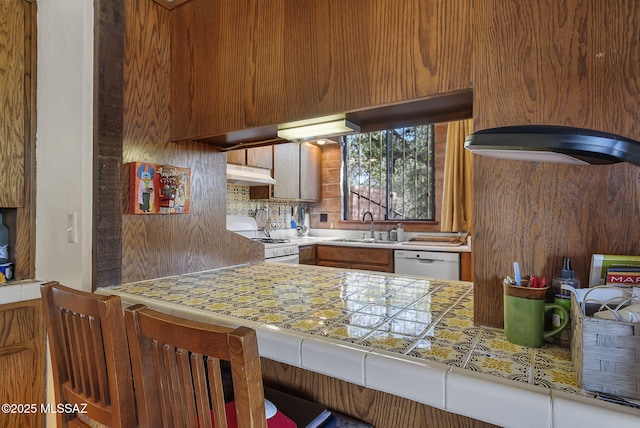 kitchen featuring light countertops, tasteful backsplash, white appliances, under cabinet range hood, and a sink