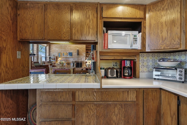 kitchen with light countertops, white microwave, brown cabinets, and decorative backsplash
