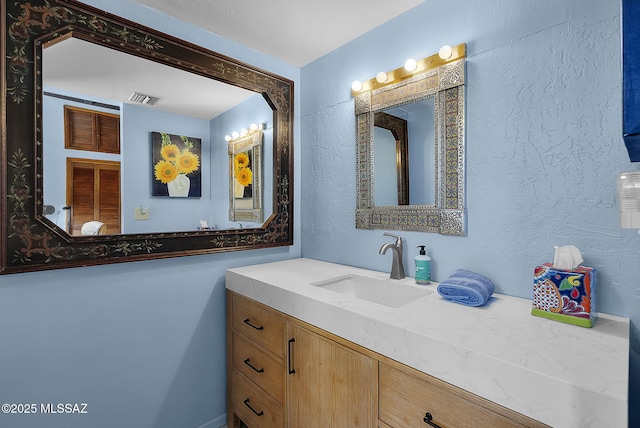 bathroom featuring visible vents, vanity, and a textured wall