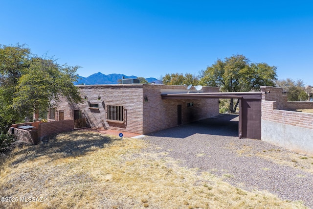 rear view of house featuring gravel driveway, an attached carport, a mountain view, and fence