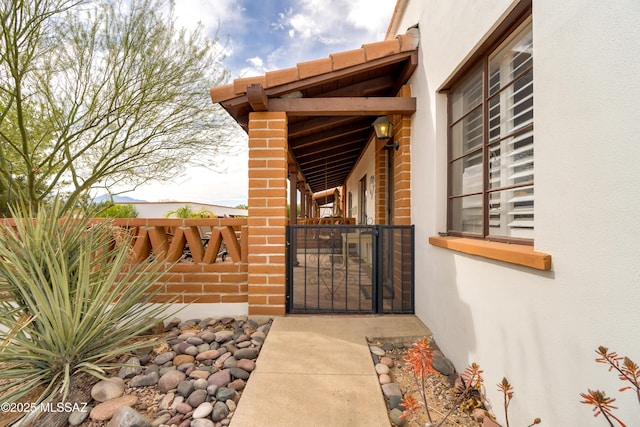 view of exterior entry with fence, a gate, and stucco siding