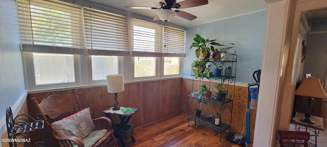 living area featuring wood finished floors, wood walls, ceiling fan, and wainscoting