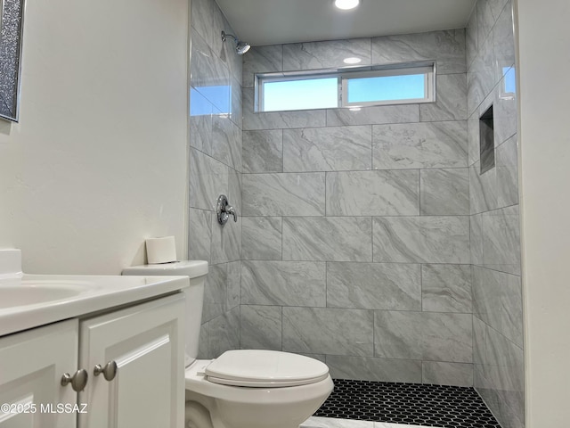 bathroom with toilet, a tile shower, and vanity