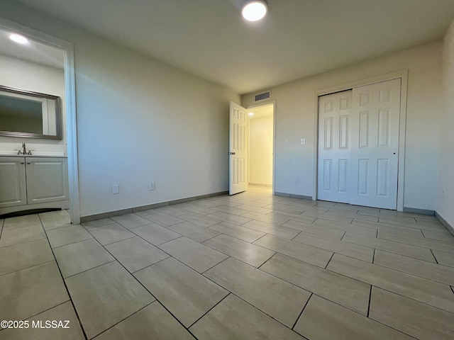 unfurnished bedroom with a sink, baseboards, a closet, and visible vents