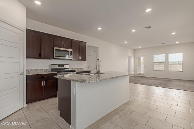 kitchen with recessed lighting, light tile patterned floors, stainless steel appliances, a center island with sink, and light stone countertops
