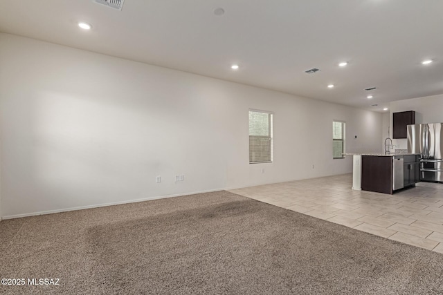 unfurnished living room featuring light colored carpet, recessed lighting, a sink, and light tile patterned floors