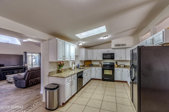 kitchen with vaulted ceiling with skylight, a sink, open floor plan, light tile patterned floors, and black appliances