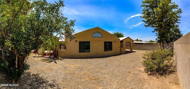 rear view of house with stucco siding and fence