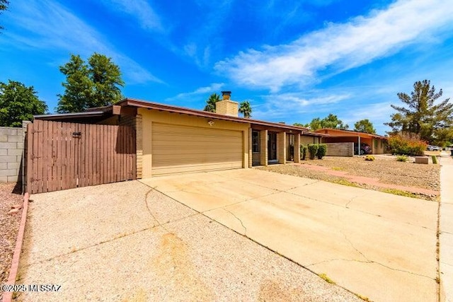 view of front facade featuring a chimney, concrete driveway, fence, and an attached garage