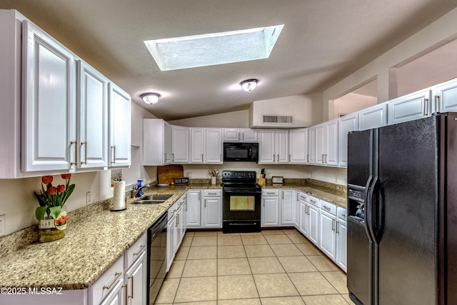 kitchen with light tile patterned floors, lofted ceiling with skylight, a sink, white cabinets, and black appliances