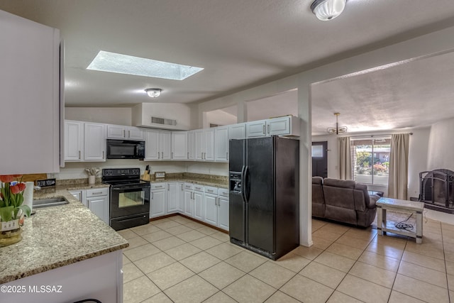 kitchen with vaulted ceiling with skylight, white cabinetry, light tile patterned floors, visible vents, and black appliances