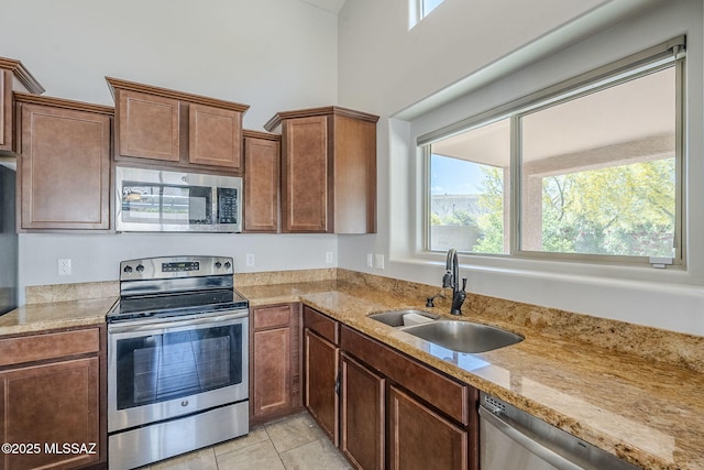 kitchen featuring light tile patterned floors, light stone counters, stainless steel appliances, and a sink
