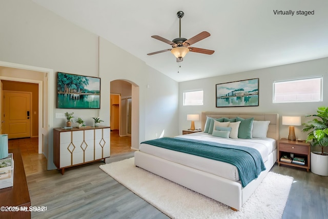 bedroom with lofted ceiling, a ceiling fan, wood finished floors, and arched walkways
