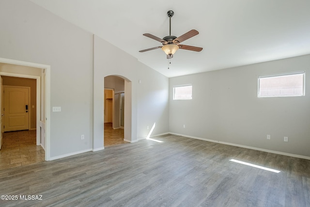 empty room with arched walkways, wood finished floors, baseboards, and ceiling fan