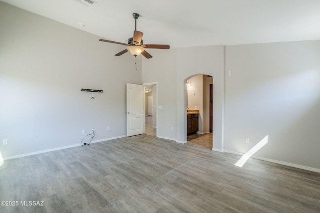 unfurnished room with ceiling fan, arched walkways, light wood finished floors, and baseboards