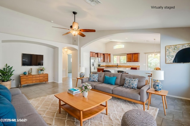 living area with arched walkways, vaulted ceiling, baseboards, visible vents, and ceiling fan