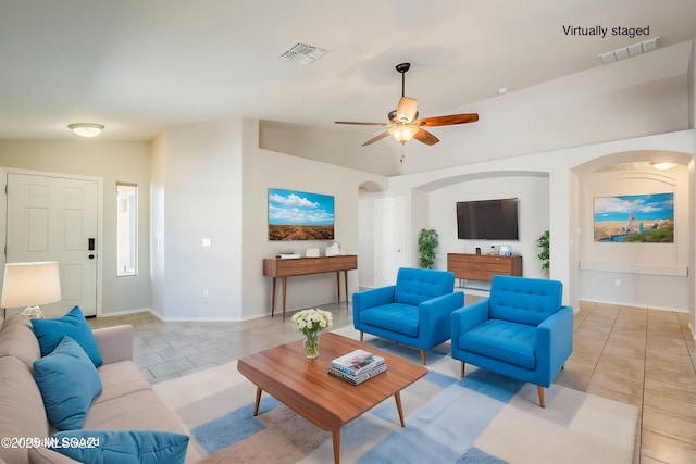 living area featuring a ceiling fan, arched walkways, light tile patterned flooring, and visible vents
