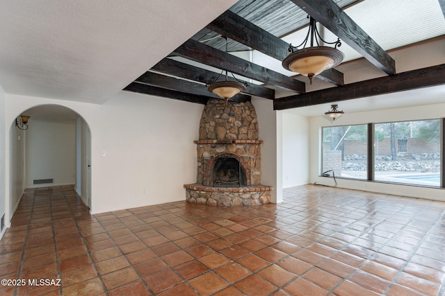 5374 E Spring Rd, Hereford, AZ 85615 - unfurnished living room with visible vents, a stone fireplace, arched walkways, beam ceiling, and tile patterned flooring
