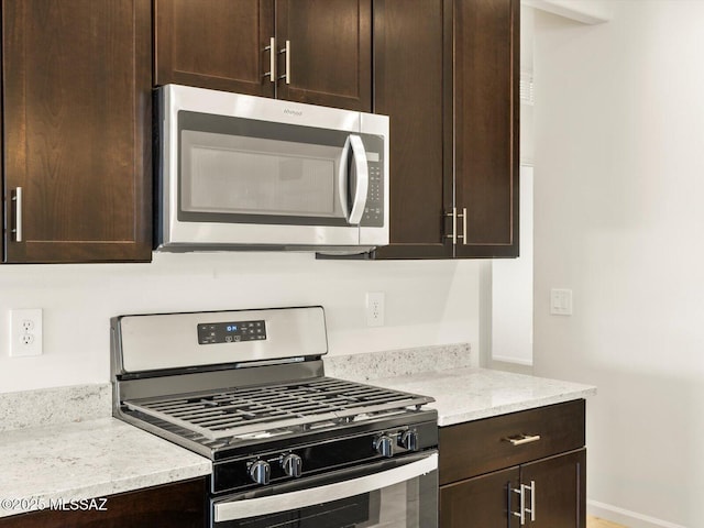 kitchen featuring dark brown cabinetry, baseboards, stainless steel appliances, and light stone counters