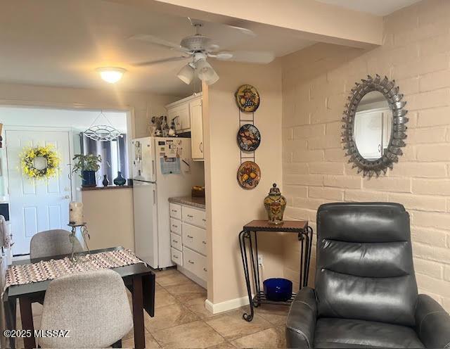 interior space with a ceiling fan, brick wall, light tile patterned floors, baseboards, and beamed ceiling