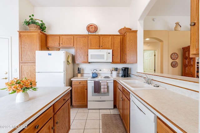 kitchen with light tile patterned flooring, white appliances, light countertops, brown cabinets, and a sink
