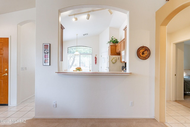 hall with visible vents, lofted ceiling, light tile patterned floors, and light colored carpet