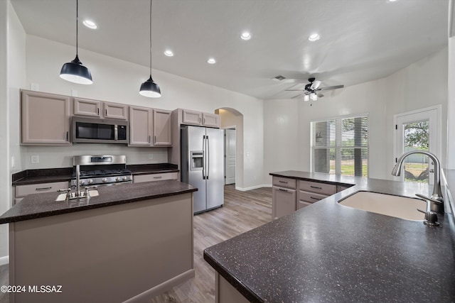 kitchen with an island with sink, a sink, a ceiling fan, stainless steel appliances, and arched walkways