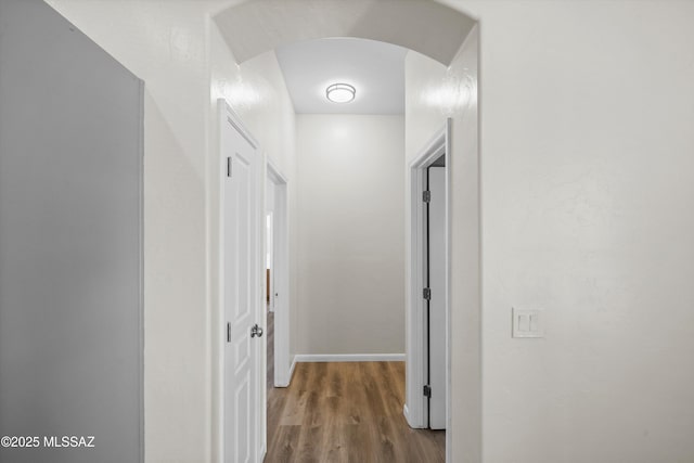 hall featuring arched walkways, baseboards, and wood finished floors
