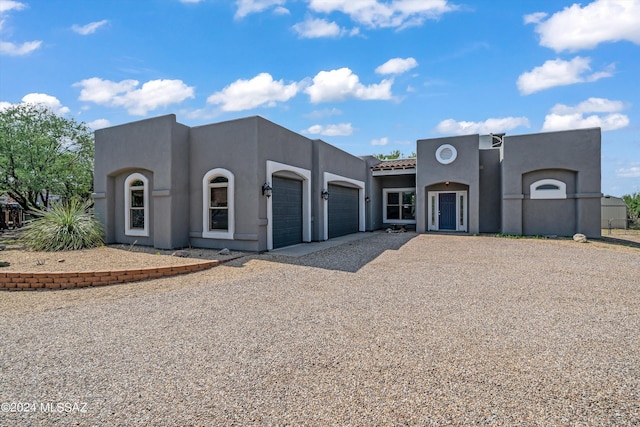pueblo revival-style home featuring driveway, stucco siding, a tile roof, and a garage