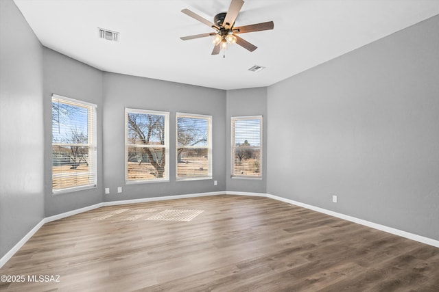 empty room featuring wood finished floors, a wealth of natural light, and visible vents