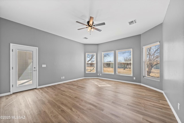 empty room featuring wood finished floors, a healthy amount of sunlight, ceiling fan, and visible vents