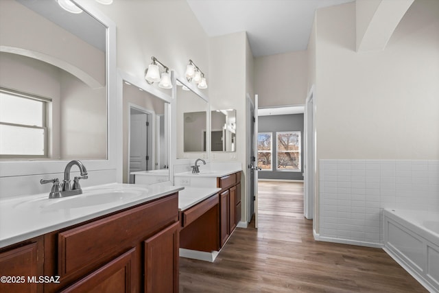 bathroom featuring a sink, a bath, two vanities, and wood finished floors