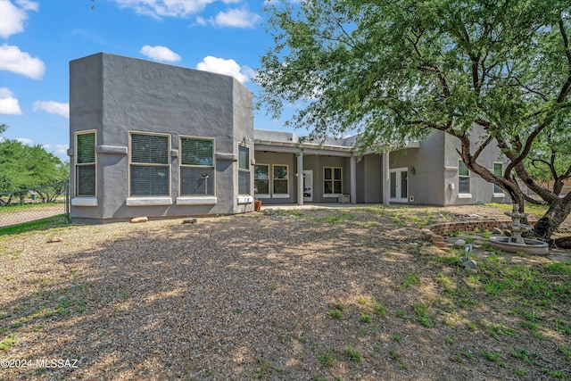 rear view of property featuring stucco siding, fence, and french doors