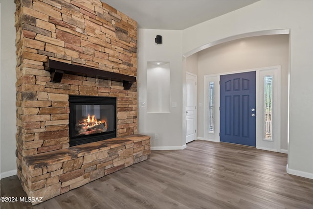 foyer entrance featuring arched walkways, baseboards, a fireplace, and wood finished floors