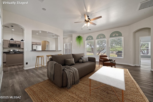 living room featuring visible vents, arched walkways, ceiling fan, and dark wood-style flooring