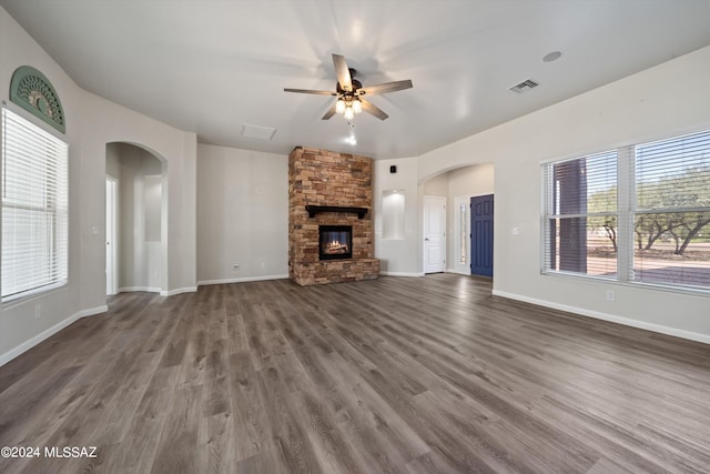 unfurnished living room with a fireplace, wood finished floors, arched walkways, and ceiling fan