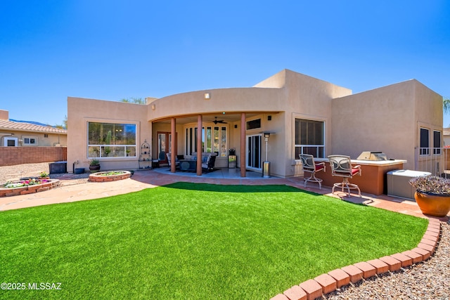 rear view of property featuring a patio, a yard, stucco siding, and ceiling fan