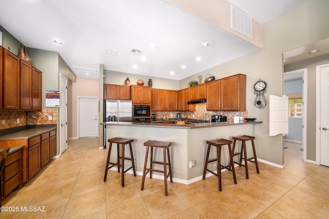 kitchen featuring a breakfast bar, a peninsula, stainless steel refrigerator with ice dispenser, under cabinet range hood, and visible vents