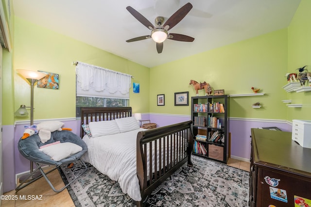 tiled bedroom with wainscoting and a ceiling fan