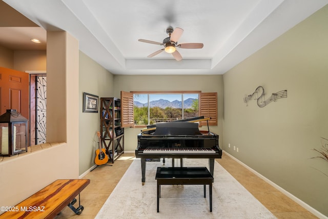 living area with tile patterned flooring, baseboards, a ceiling fan, and a raised ceiling