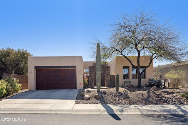 pueblo-style house with stucco siding, a garage, concrete driveway, and fence