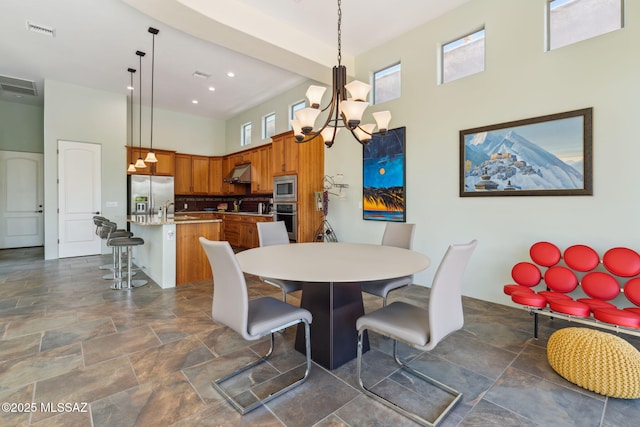 dining space featuring visible vents, a notable chandelier, a towering ceiling, and stone finish flooring