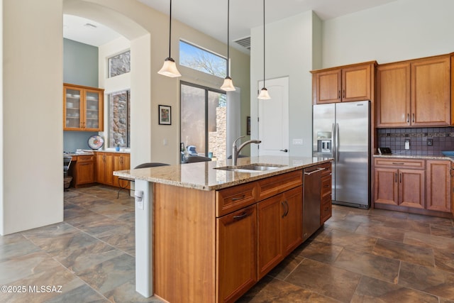kitchen featuring arched walkways, a sink, brown cabinets, and appliances with stainless steel finishes